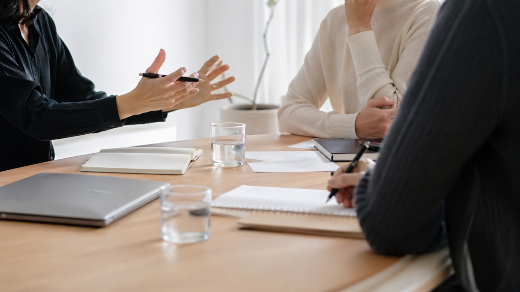 Personnes échangeant autour d’une table avec un ordinateur en appui, pour illustrer la place humaine dans l’usage de l’IA.